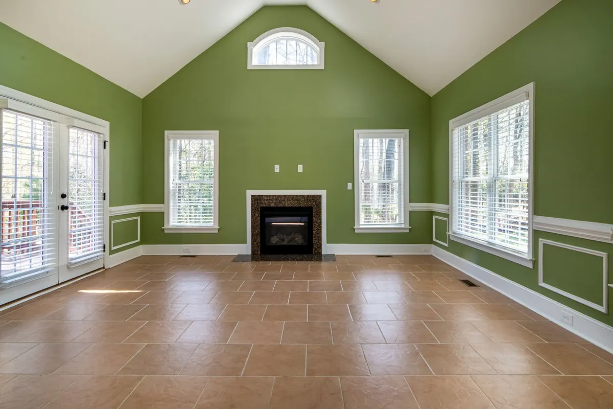 A large empty living room with olive-green walls, white trim and windows, a fireplace and a tiled floor