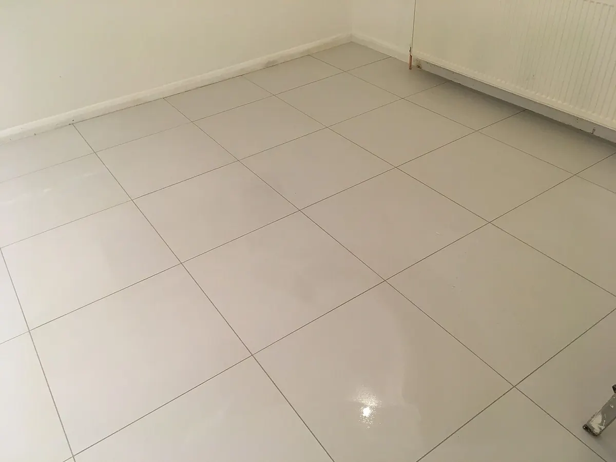 A floor of large, pale grey porcelain tiles with thin grout lines meeting at a wall
