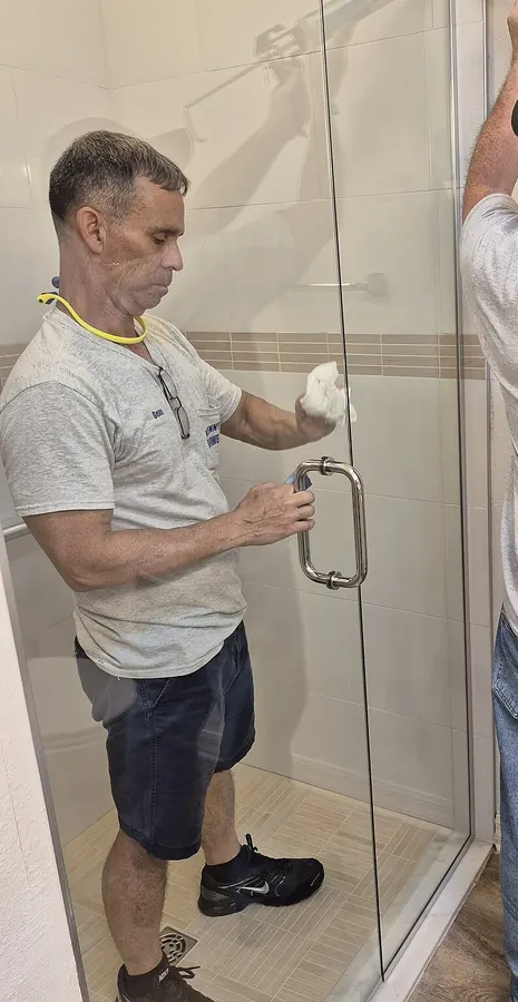 An installer finishing a frameless glass shower door in a tiled shower stall