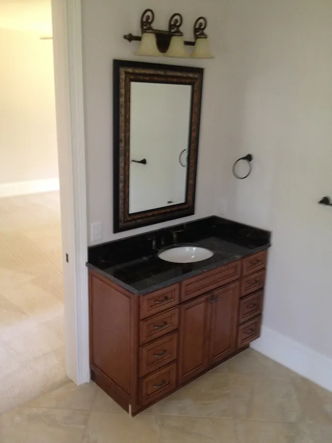 A finished bathroom vanity with a stone top, framed mirror and wall lights