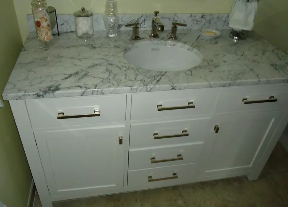 A white shaker-style bathroom vanity with five drawers, two doors, brushed nickel pulls and a white marble top with an undermount sink