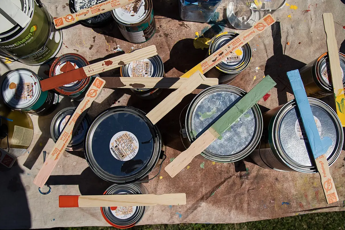 Open and closed paint cans with wooden stir sticks on a paint-spattered drop cloth