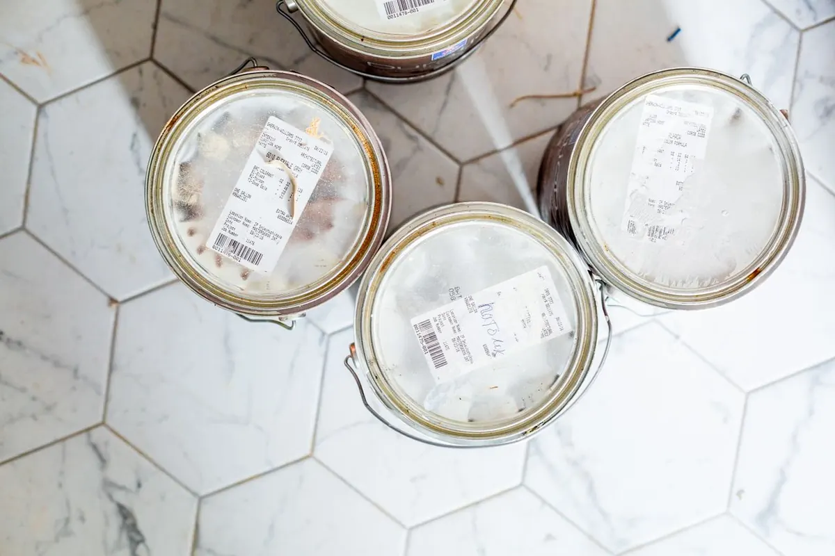 Four one-gallon paint cans with store tags seen from above on a white hexagonal tile floor