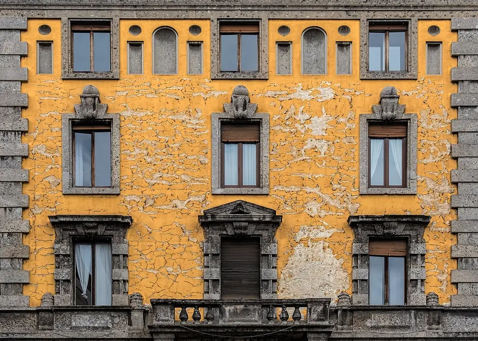 Peeling ochre plaster facade with stone window surrounds on an apartment building near the Duomo in Milan
