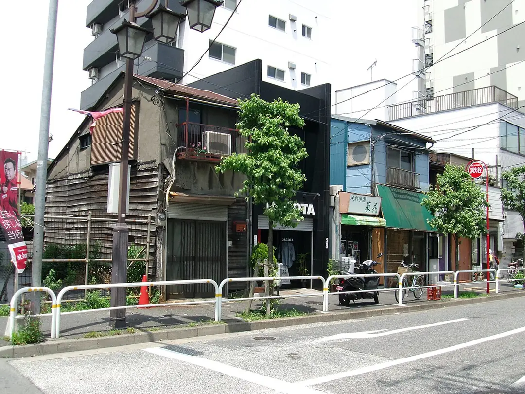 Narrow street in Tokyo with a worn wooden building next to newer concrete and painted buildings