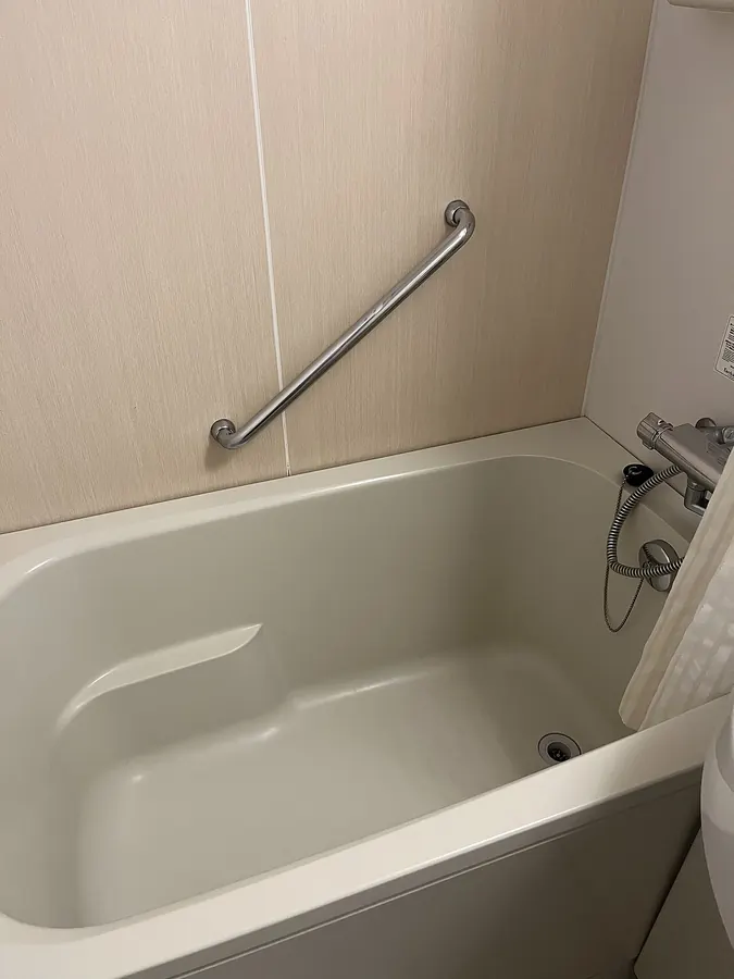 Compact molded plastic bathtub with a handrail and a thermostatic faucet