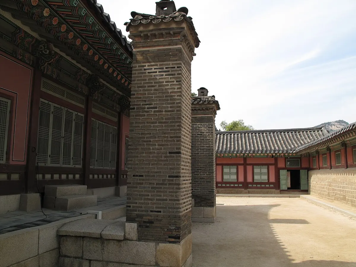 Two tall brick chimneys rising beside a palace building with a tiled roof