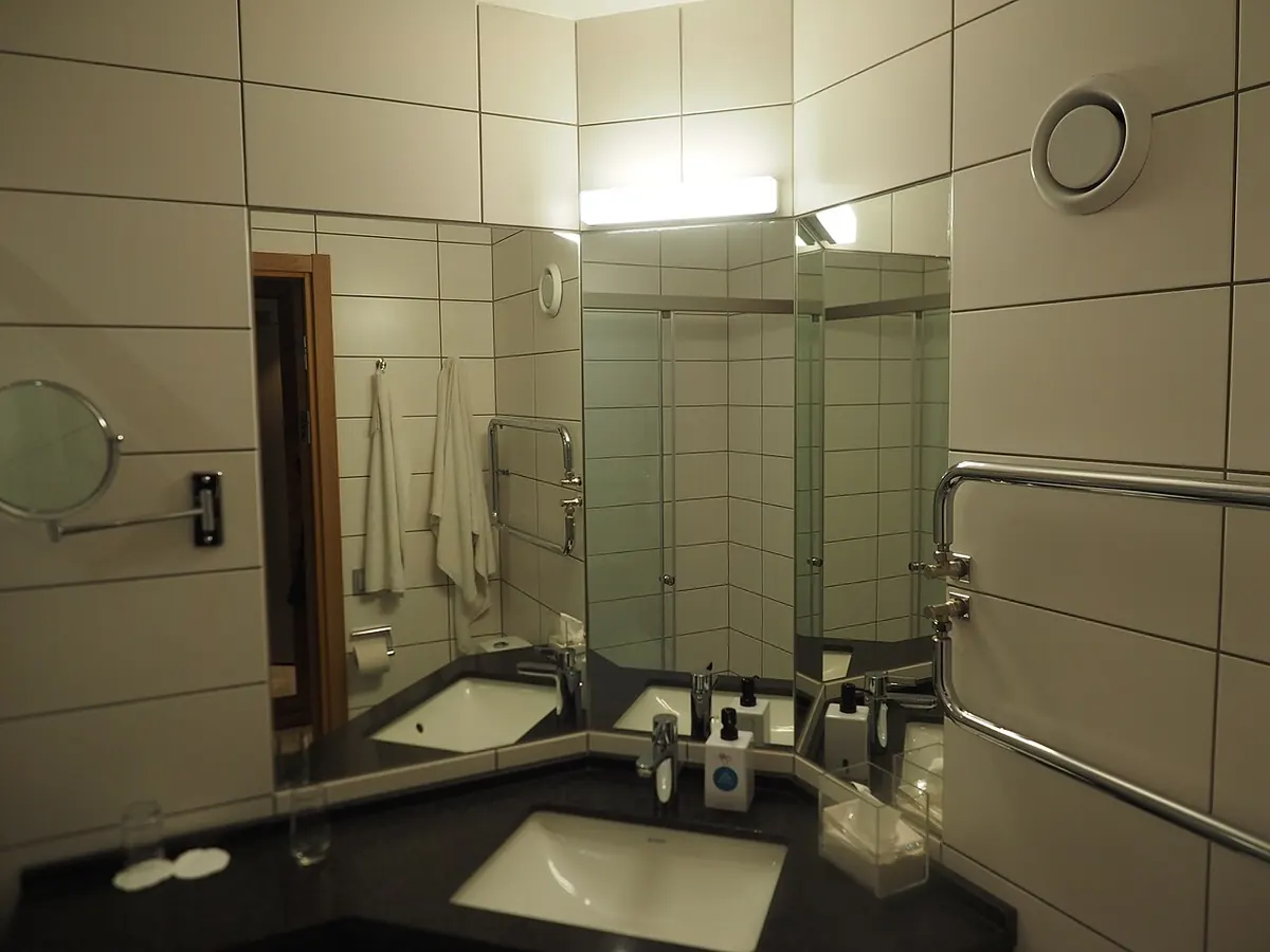 A tiled hotel bathroom in Borås, Sweden, with large wall tiles, a mirrored corner vanity, a glass shower and a chrome heated towel rail