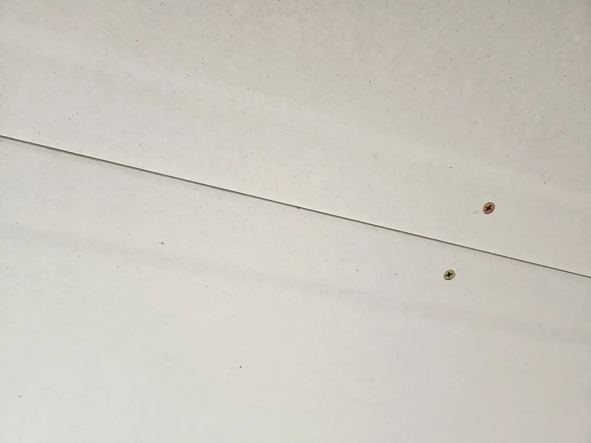Close-up of two drywall sheets meeting at a horizontal seam with screws along the tapered edges
