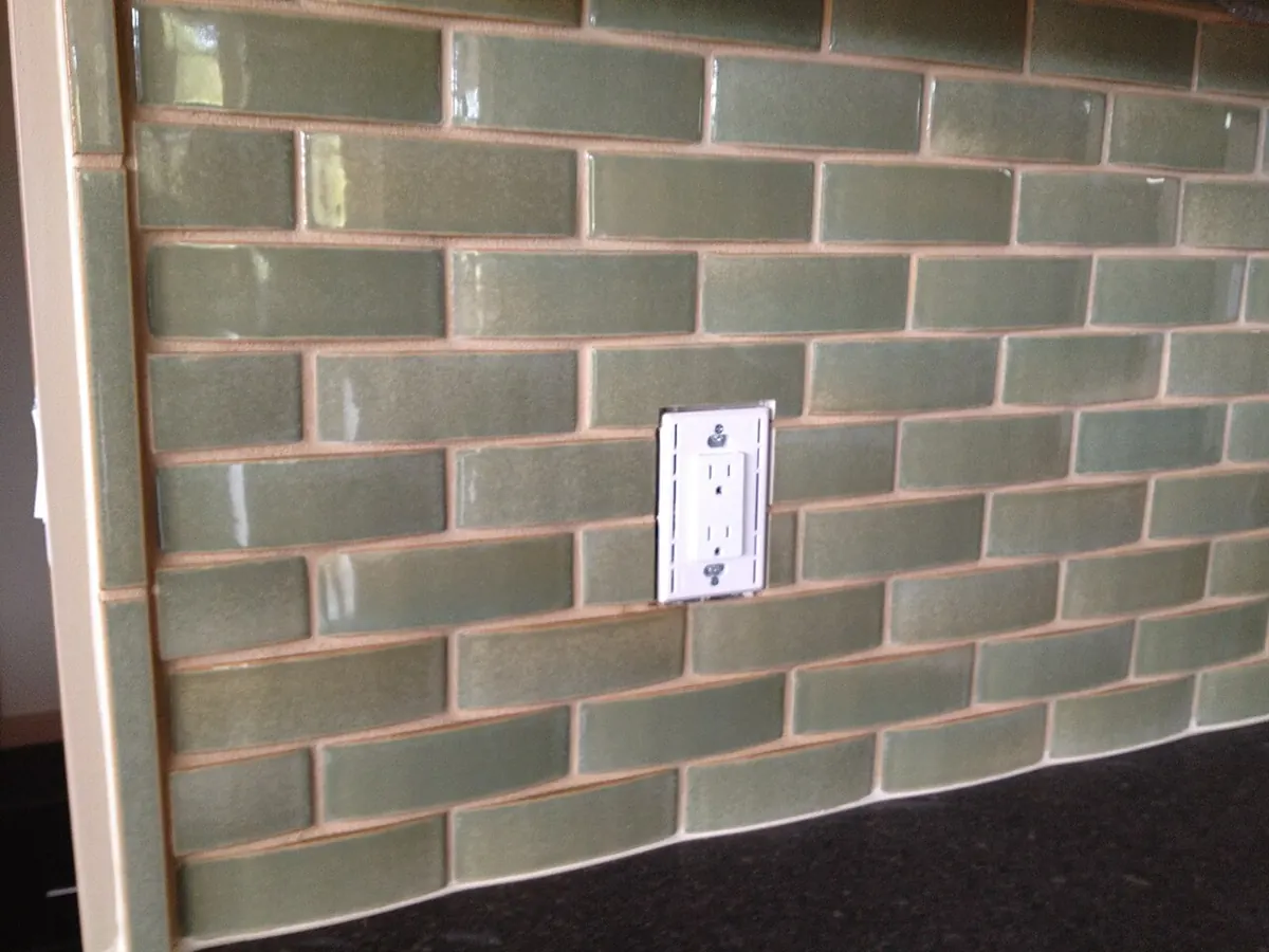 Green glazed subway-style backsplash tile with a white outlet cut into the field