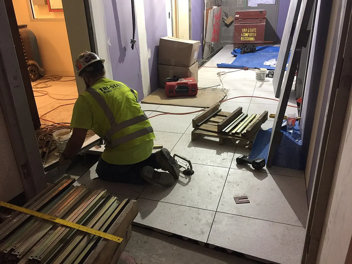 Installer kneeling on a floor of large pale tiles with a yellow tape measure in the foreground