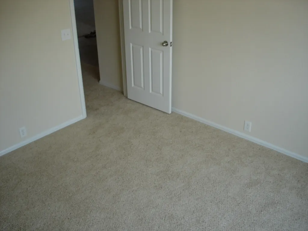 White baseboard running along a beige wall and stopping at the casing of an open bedroom door