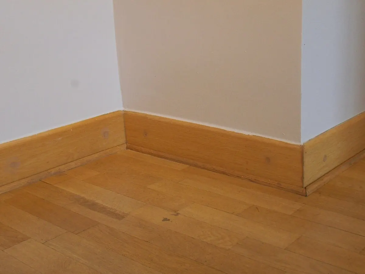 Oak baseboard on a wood floor turning an inside corner and wrapping around an outside corner of a wall