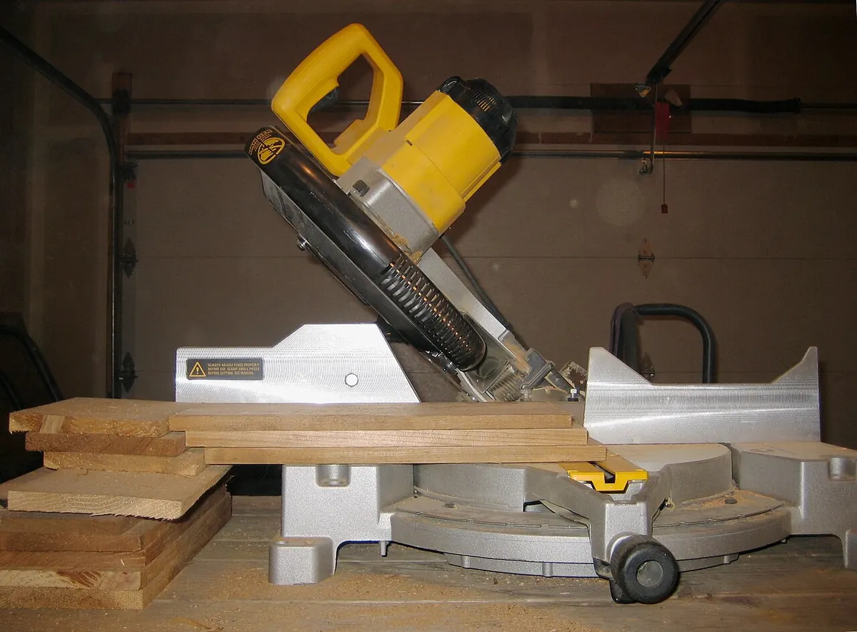 Sliding compound miter saw on a workbench with a stack of thin wood boards on the table