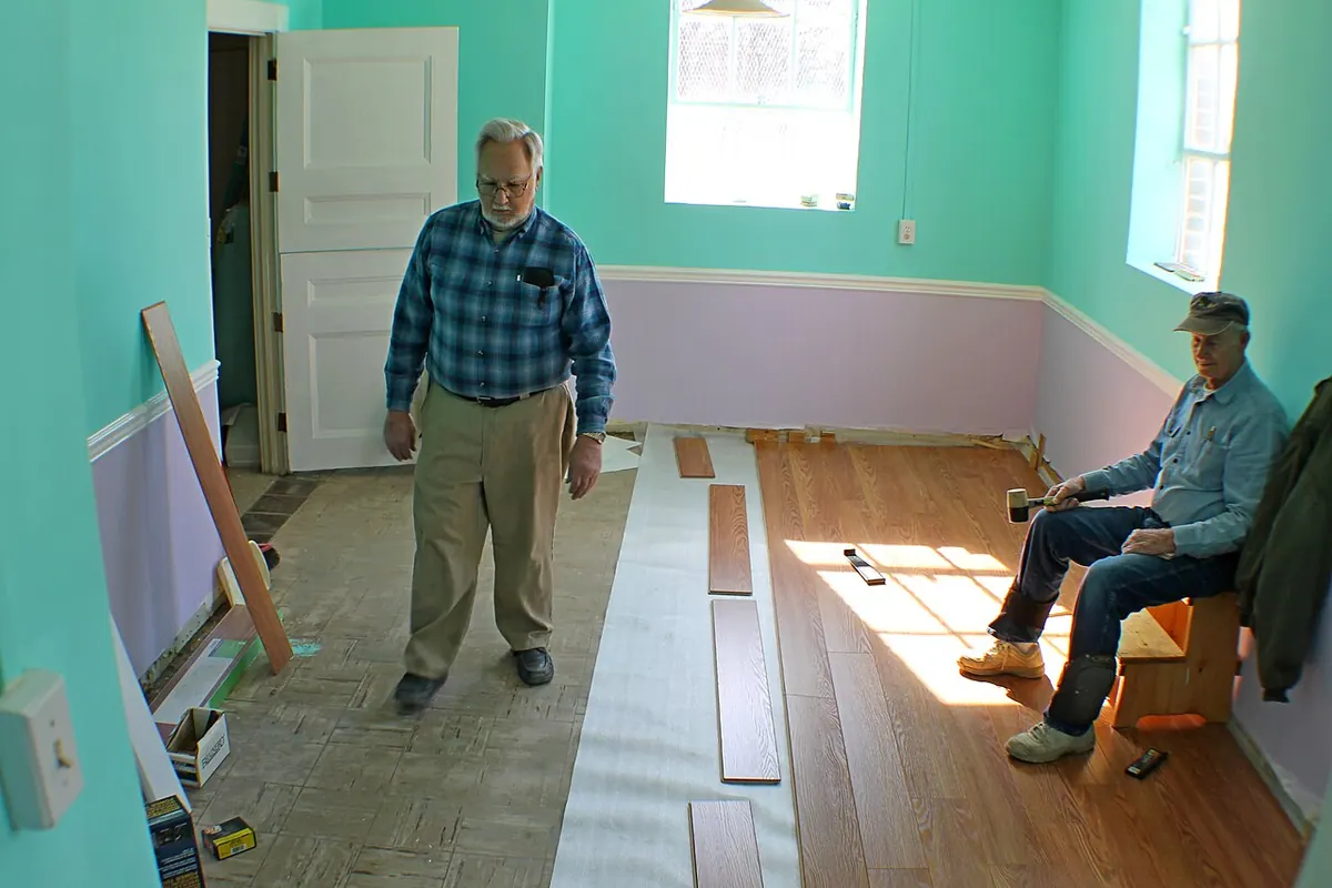 White underlayment strips rolled out over an old floor, with the first rows of wood-look laminate planks fitted on top
