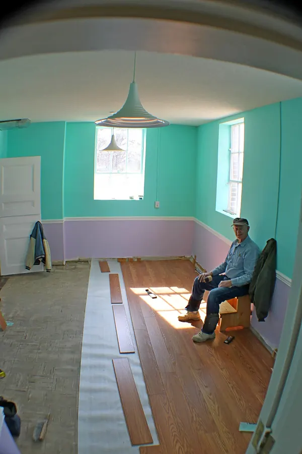 An unfinished room with long white strips of underlayment rolled out across the old floor and the first rows of wood-look laminate laid on top