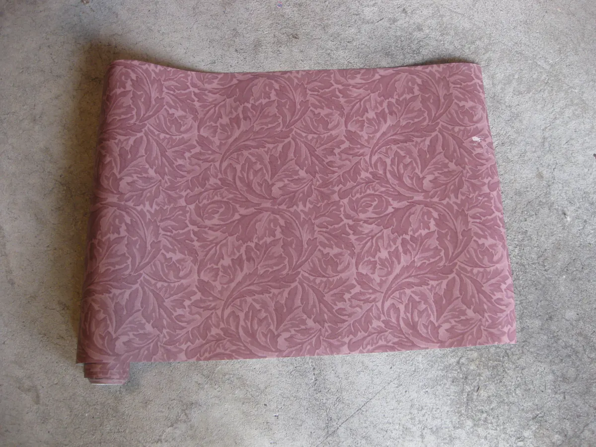 Roll of mauve wallpaper with a repeating leaf pattern partly unrolled on a concrete floor