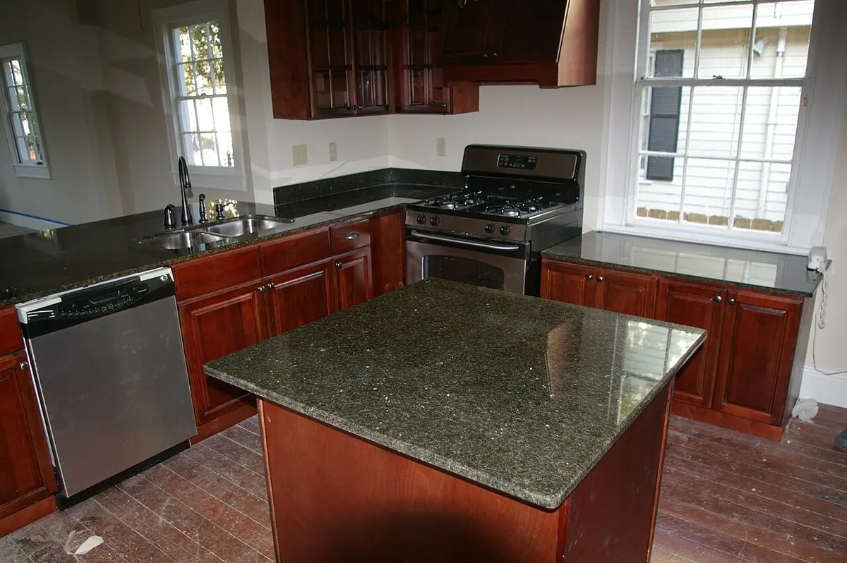 Kitchen with dark green granite on an L-shaped run of cabinets and a separate square island in front of the stove