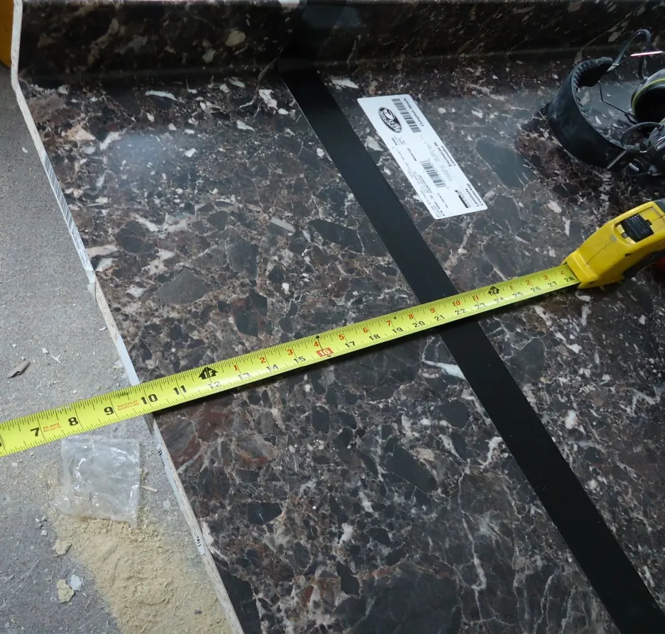 Yellow tape measure stretched across a dark laminate countertop blank on a workshop floor