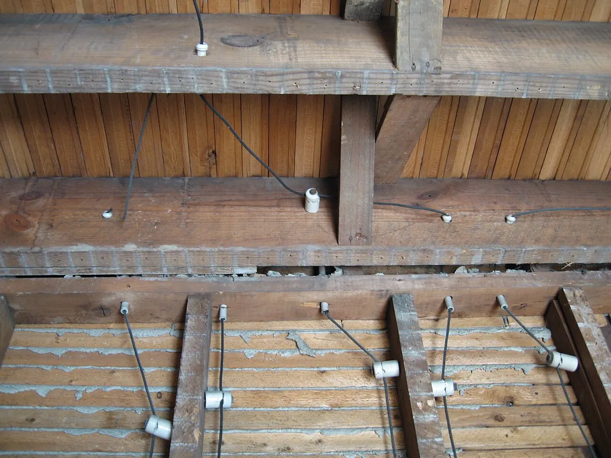 Old knob-and-tube wiring on white ceramic insulators running along exposed wooden joists and lath