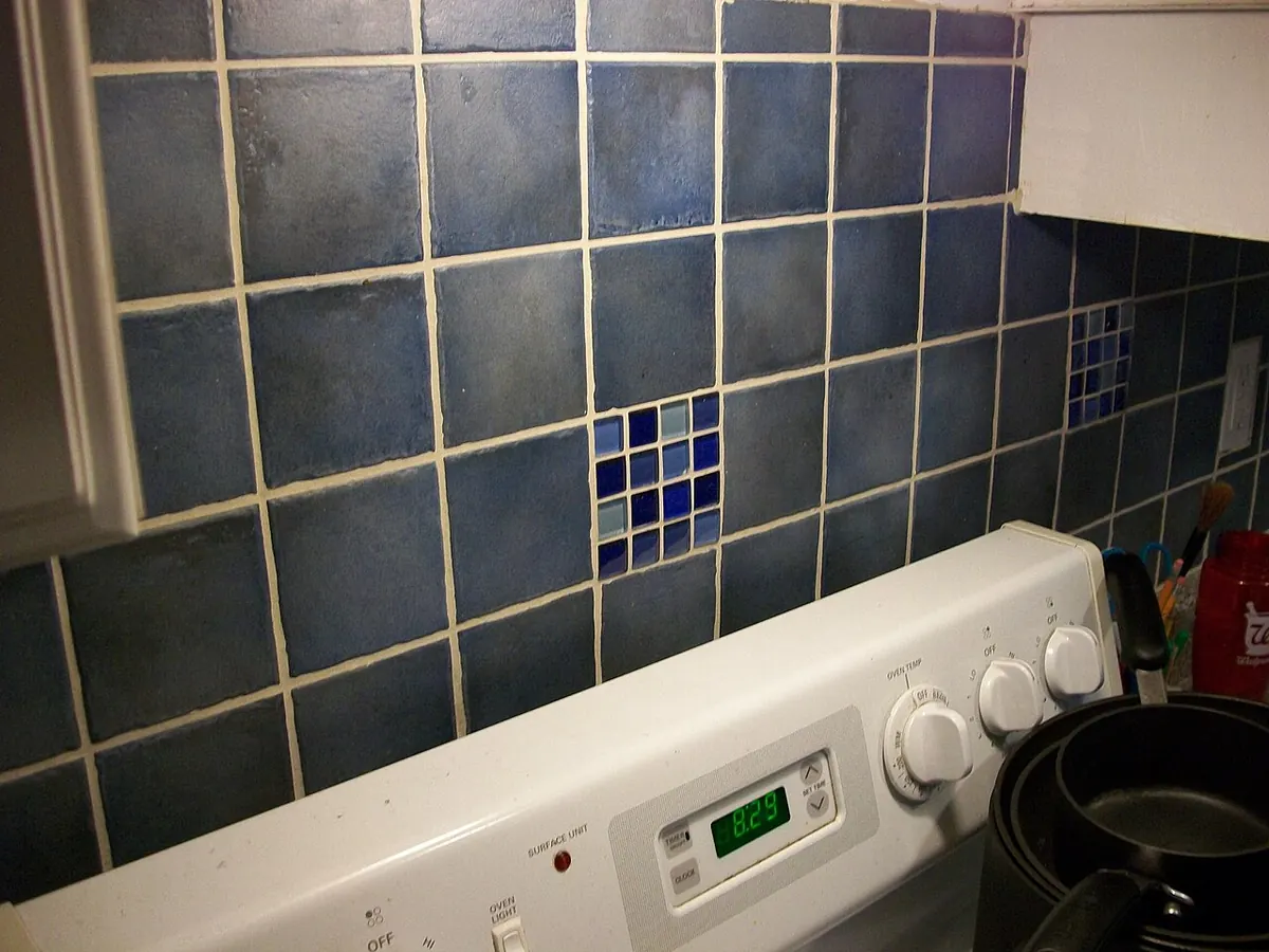 Blue square kitchen backsplash tiles with small glass mosaic inserts and visible cream grout joints above a stove