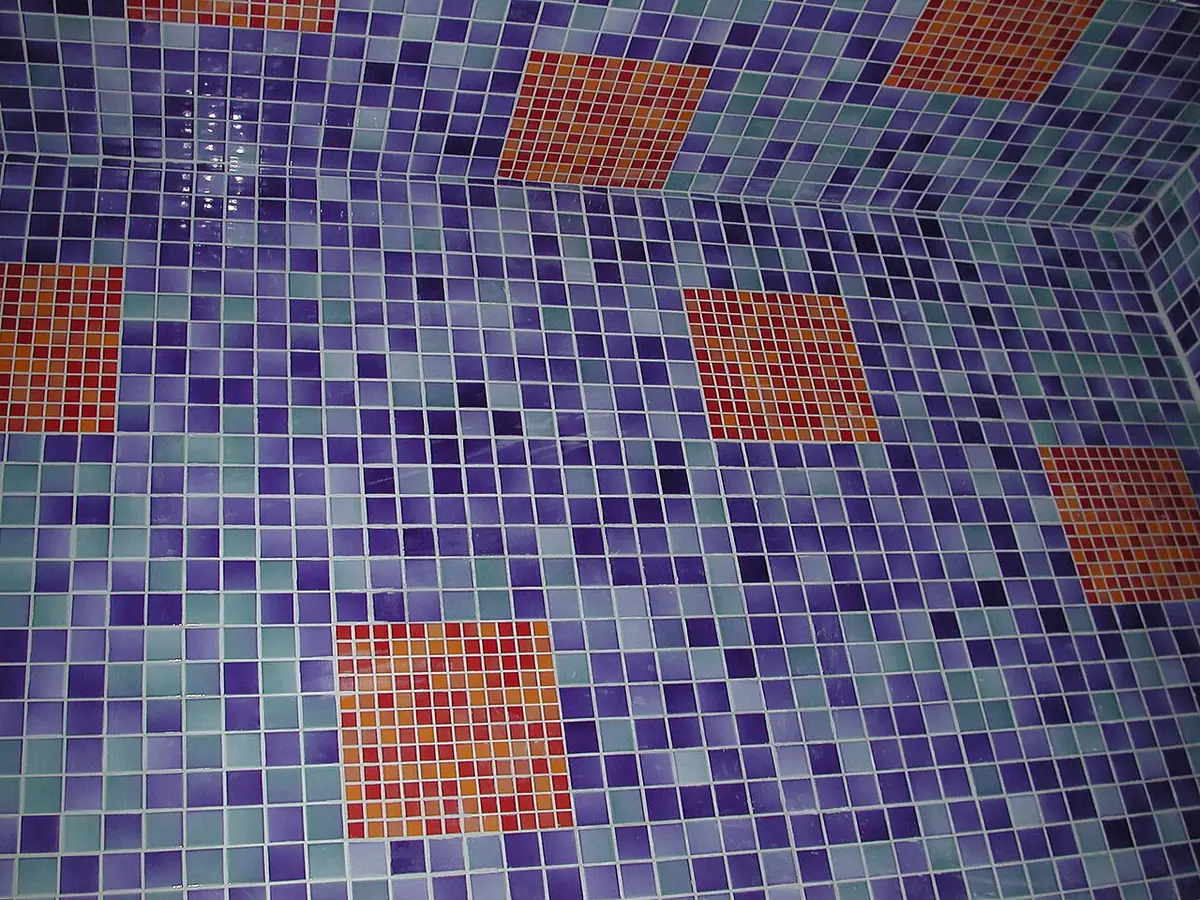 Shower floor and walls covered in small purple, teal and orange glass mosaic tiles with thin pale grout lines