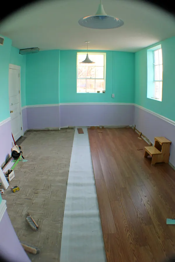 An empty room with a strip of white underlayment rolled over the old floor and new wood-look laminate already laid across half the room