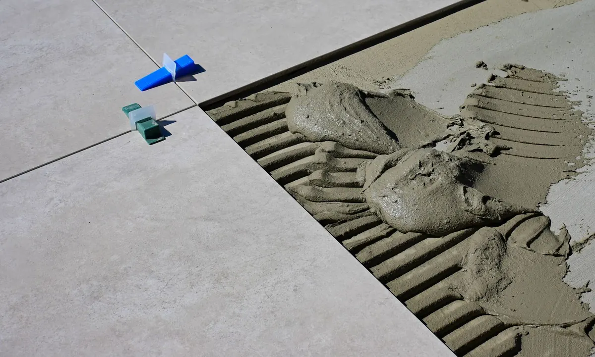 Large grey floor tiles set with plastic levelling clips beside a fresh bed of trowelled grey mortar ready for the next tile