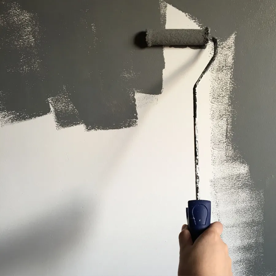 A paint roller laying a stripe of dark grey paint over a white wall, with the white showing through thin areas
